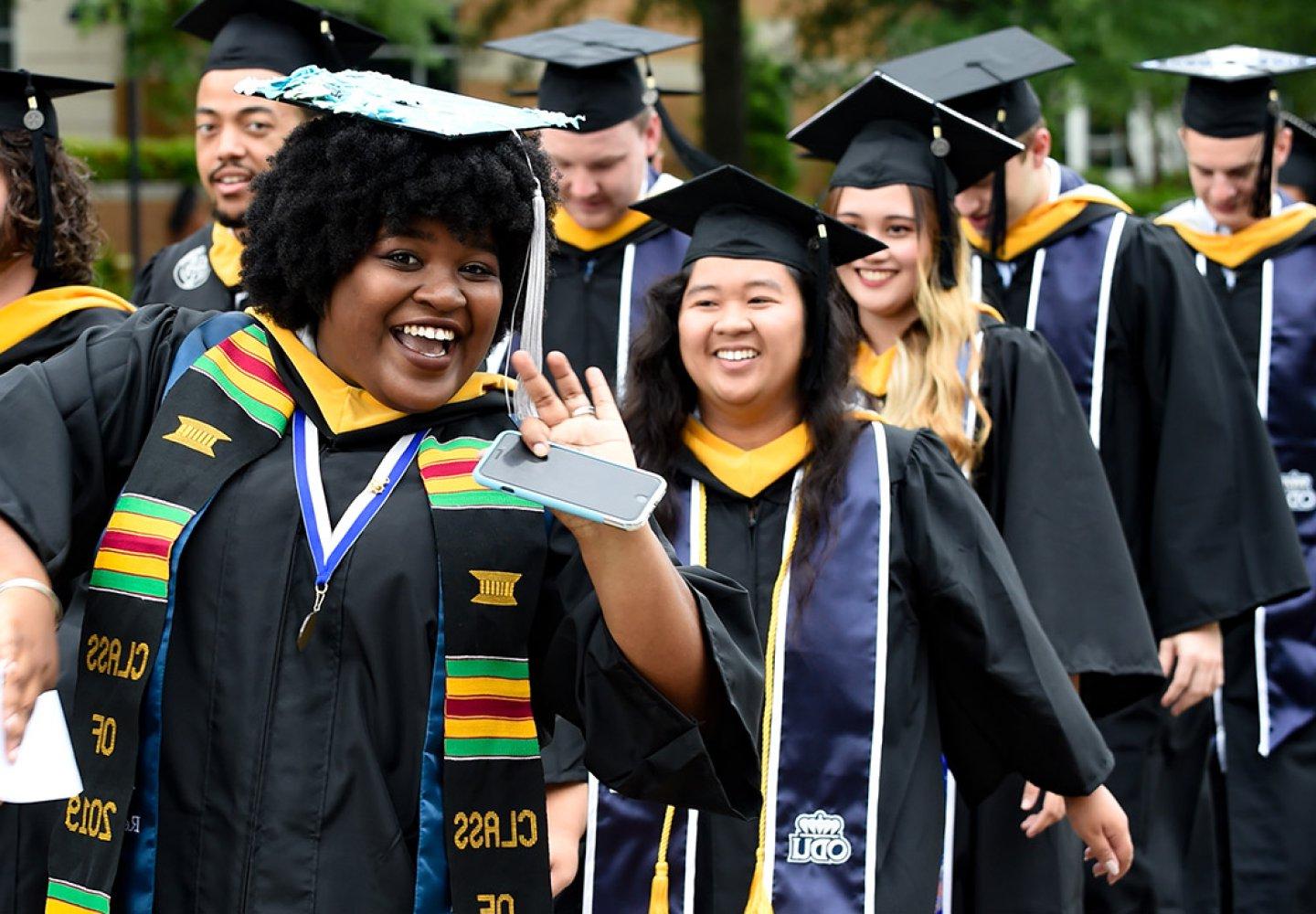 Black female graduate waves at photographer in procession